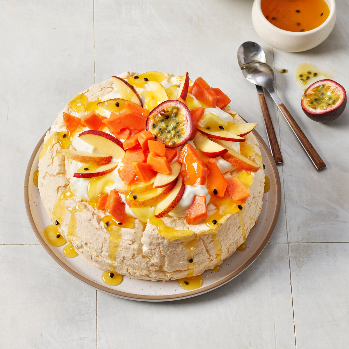 Fruit-topped dessert on a plate with a bowl of additional fruits and a cup of sauce in the background.